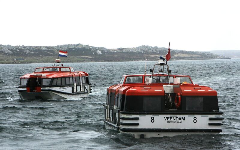 Twee oranje-witte tenderboten van een cruiseschip varen naar de steiger in de haven van Stanley