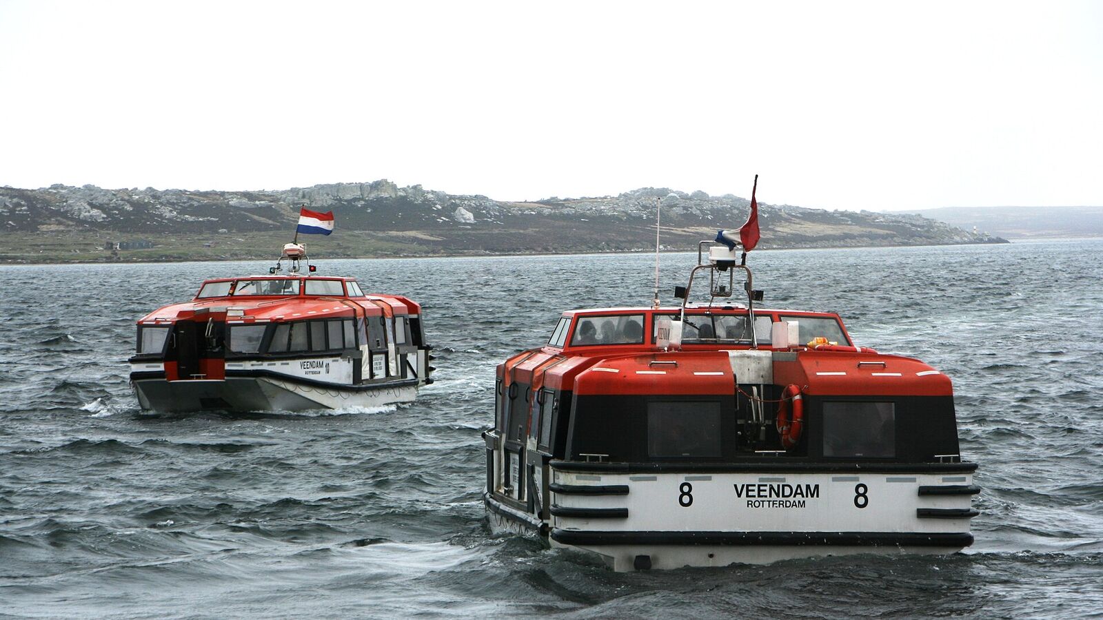 Twee oranje-witte tenderboten van een cruiseschip varen naar de steiger in de haven van Stanley
