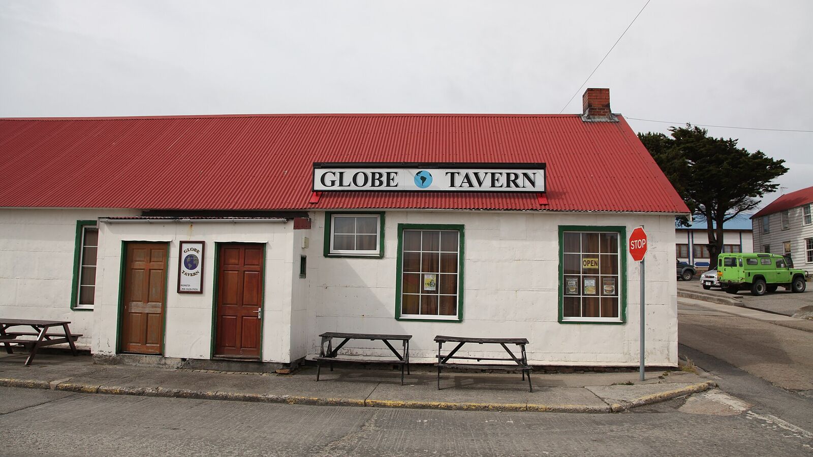 De witte Globe Tavern met rood dak en picknicktafels aan een straathoek in Stanley