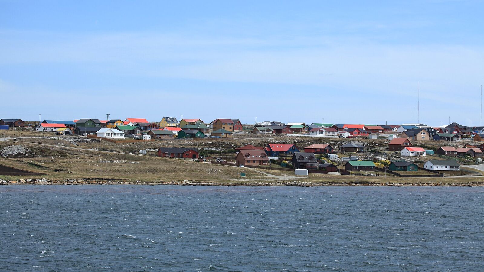 Gekleurde huizen van Stanley aan de overkant van het water van Stanley Harbour onder een blauwe lucht