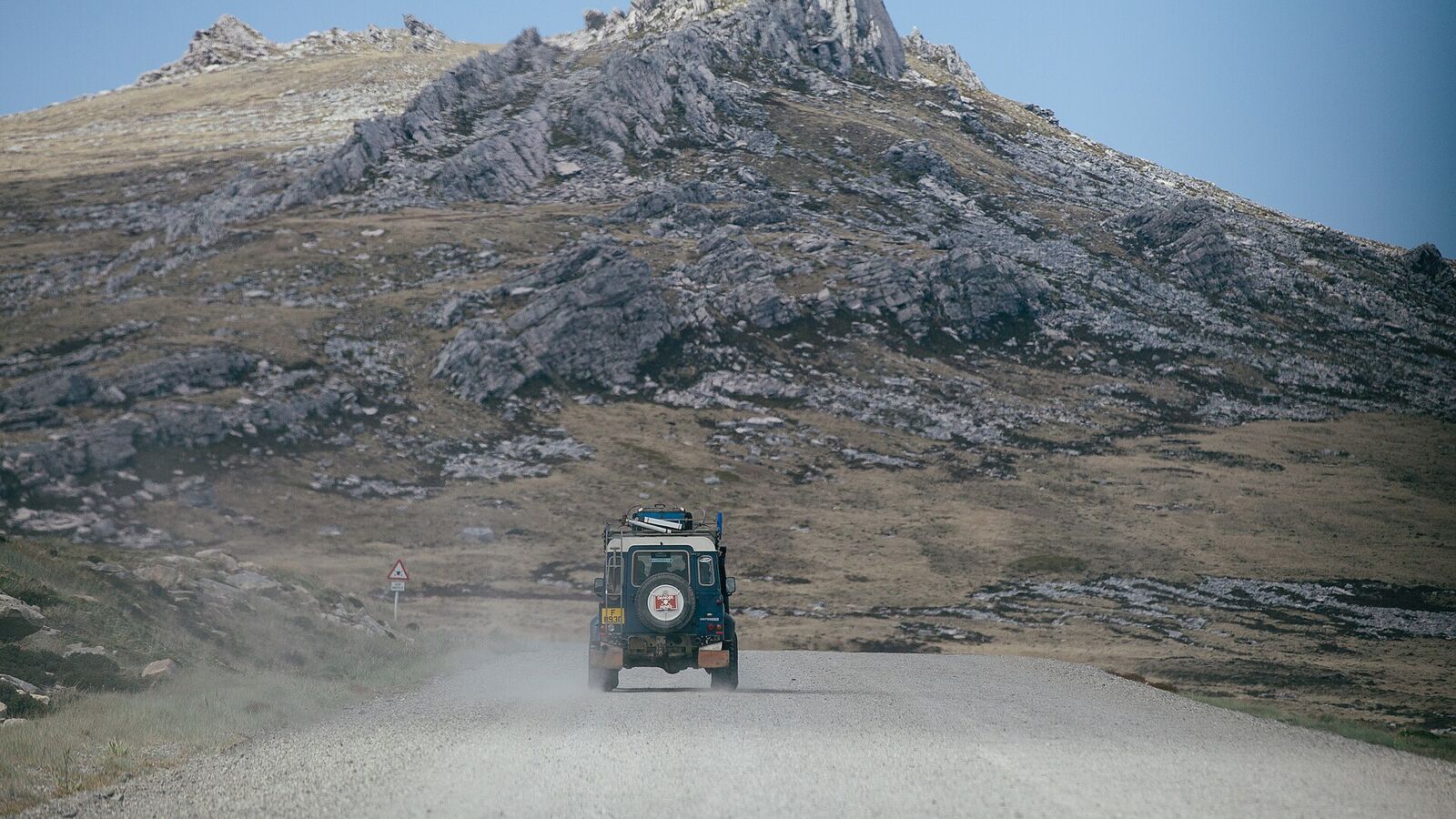 Een terreinwagen rijdt over een onverharde weg op East Falkland met een rotsachtige heuvelrug op de achtergrond