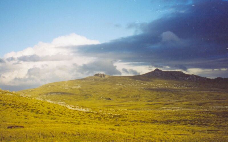Glooiend geel-groen heuvellandschap op de Falklandeilanden onder een blauwe lucht met wolken