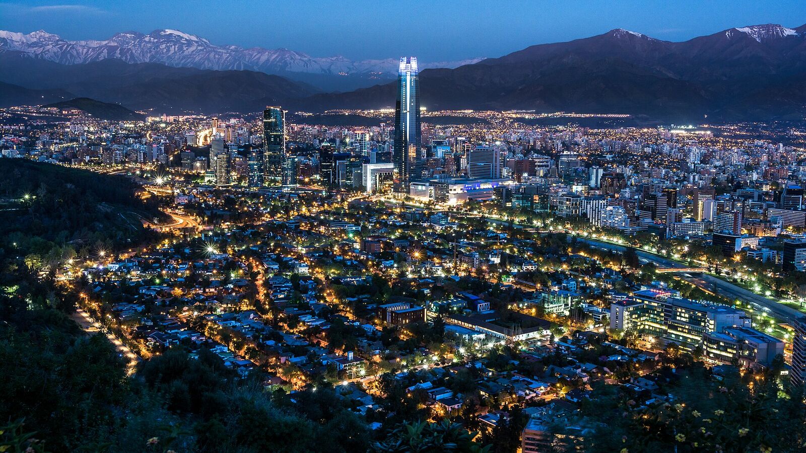 Santiago de Chile in het blauwe uur, met verlichte straten, de Gran Torre en de Andes op de achtergrond