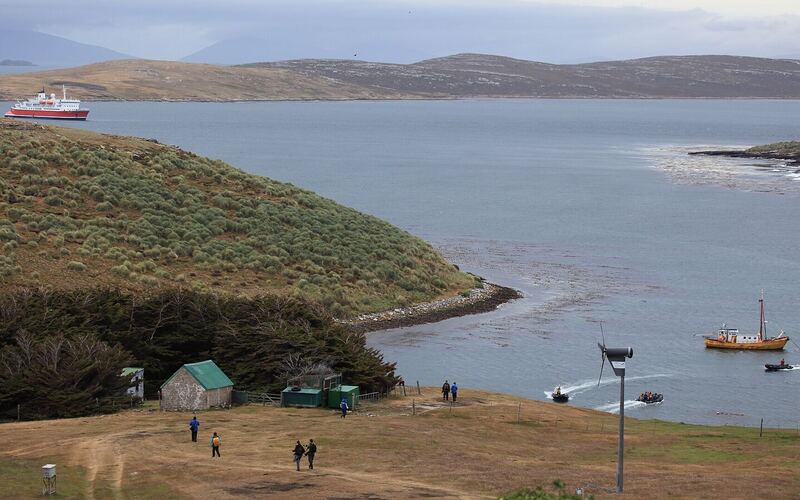 Groene heuvels en de beschutte baai van West Point Island met de settlement en een expeditieschip