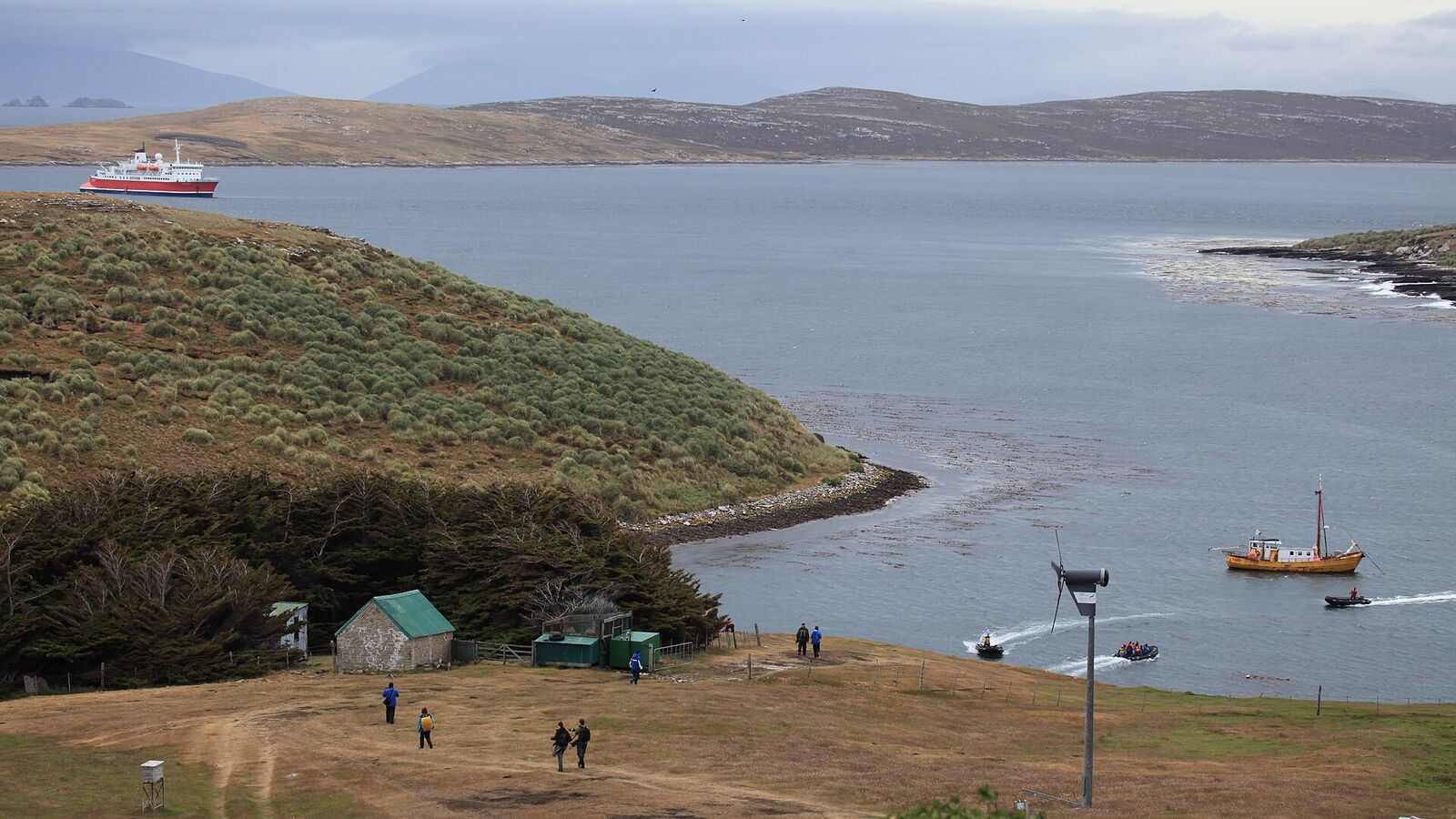 Groene heuvels en de beschutte baai van West Point Island met de settlement en een expeditieschip